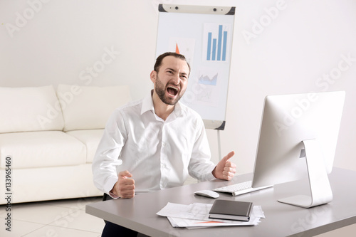 Handsome angry man sitting at table in office