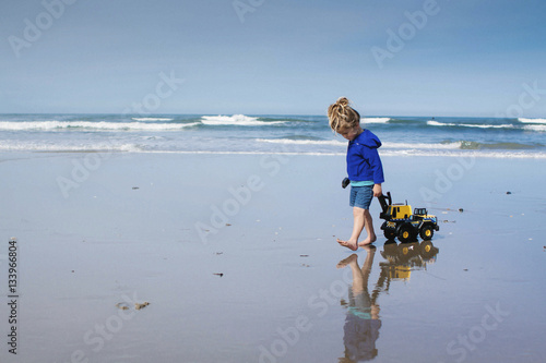 Girl pulling toy truck while walking at beach against cloudy sky photo