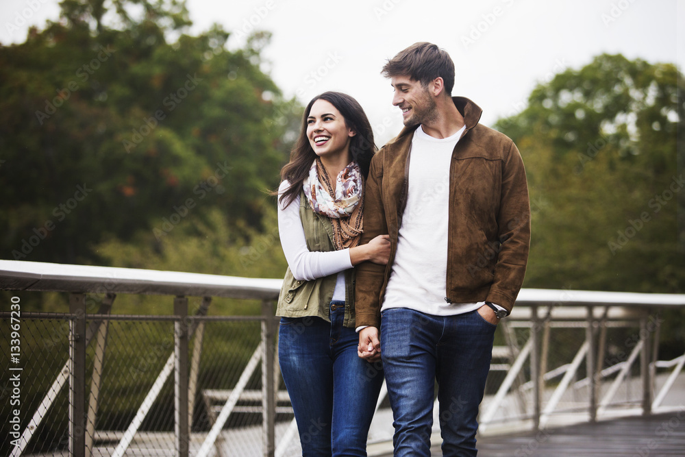 Happy couple holding hands while walking on bridge against clear sky Happy couple holding hands while walking on bridge against clear sky