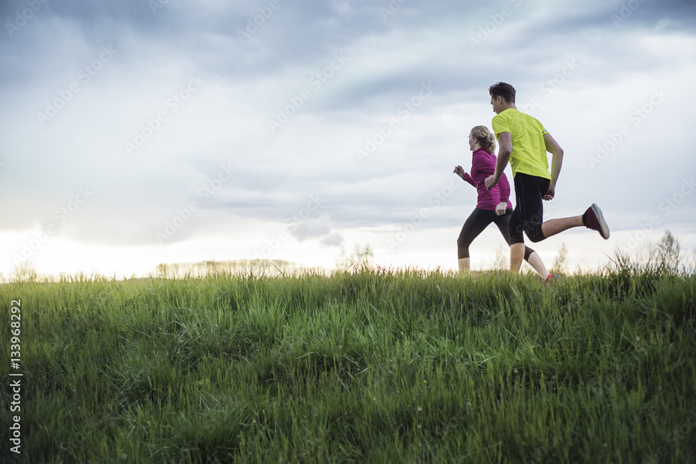 Side view of determined athletes running on grassy field against sky Side view of determined athletes running on grassy field against sky