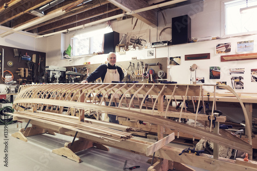 Portrait of confident senior man standing by incomplete boat in workshop