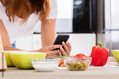 Woman Using Smartphone In Kitchen