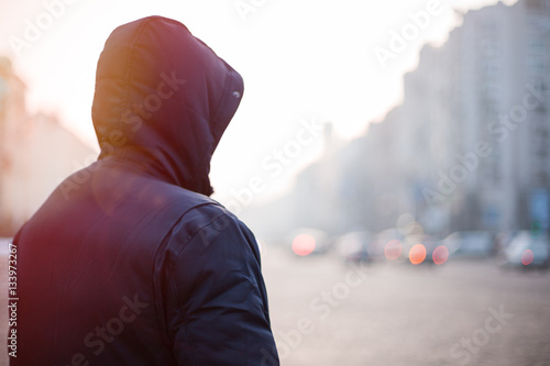 Hipster man in hood walking on city street in the evening