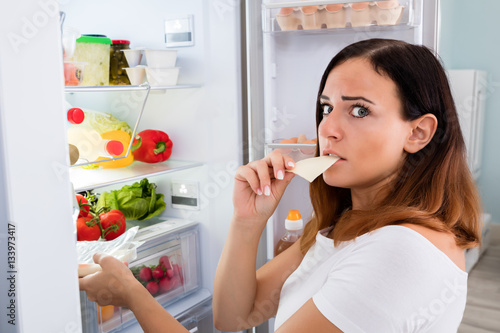 Woman Eating Cheese In Front Of Refrigerator