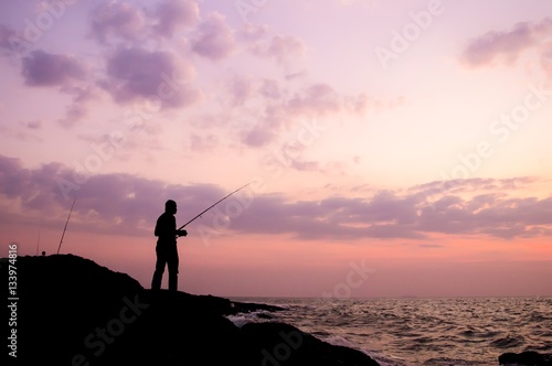 Silhouette of man fishing on the stone at seaside