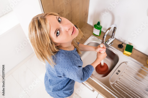Canvas Print Sad Woman Using Plunger In Kitchen Sink