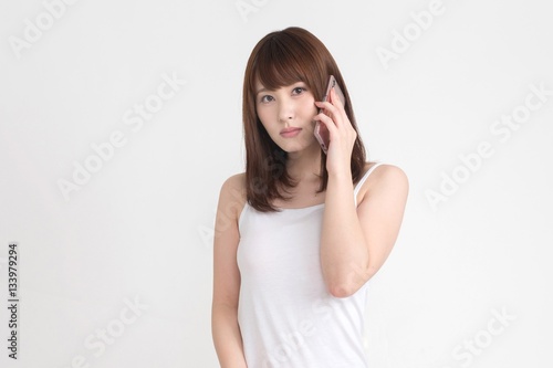 若い女性が、スマートフォンを操作しています。この画像の背景は白です。