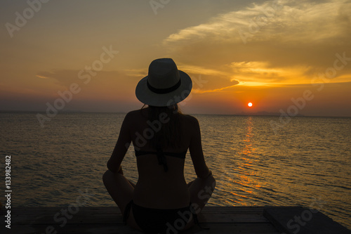 Beautiful girl in a straw hat sitting on the beach during sunset. Thailand