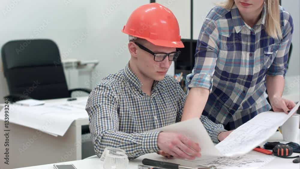 Architect working on blueprints while female colleague bringing more drawings Architect working on blueprints while female colleague bringing more drawings