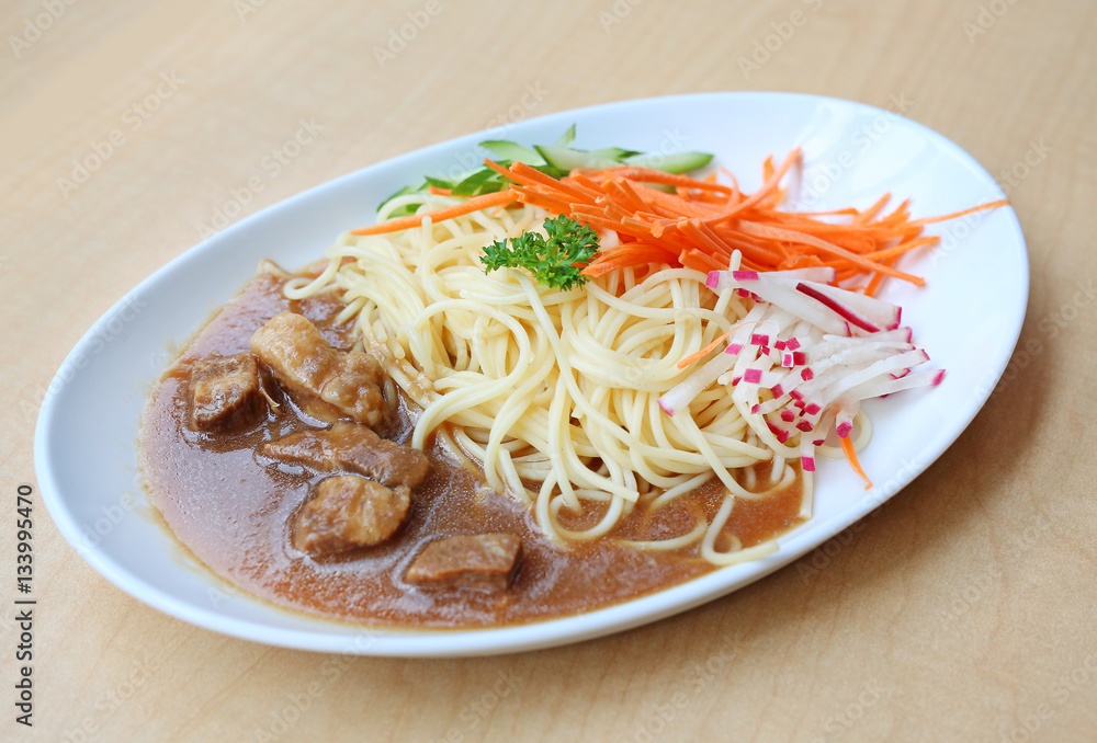 Spaghetti with steamed pork and vegetable on white plate against wooden background