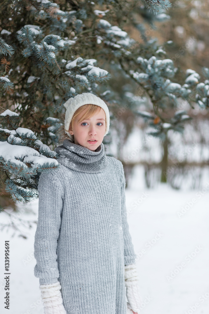Obraz premium Beautiful girl in a white hat and mittens in the winter snowy fo