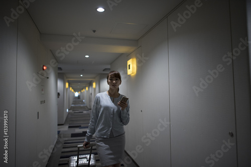 The woman is walking in the hotel corridor while watching smartphone