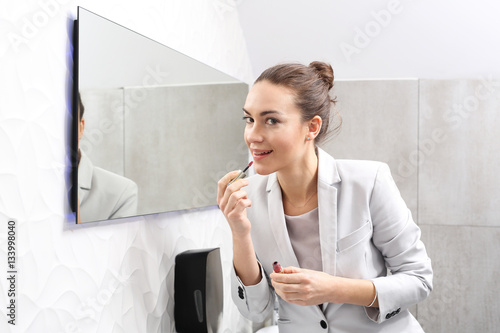 Kobieta maluje usta w biurze. Atrakcyjna kobieta biznesu maluje usta pomadką w firmowej łazience