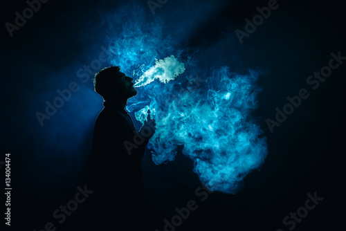 The man smoke an electronic cigarette on the background of the blue light
