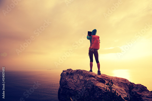 successful hiker use digital tablet taking photo on seaside mountain peak rock