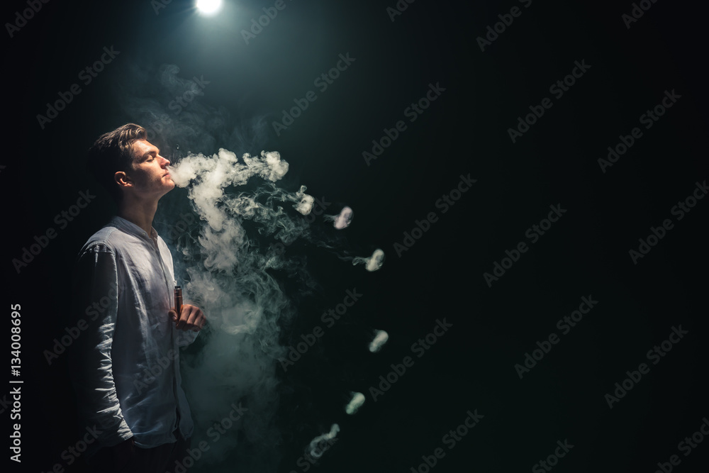 The man smoke an electric cigarette with a ring and on the dark background The man smoke an electric cigarette with a ring and on the dark background