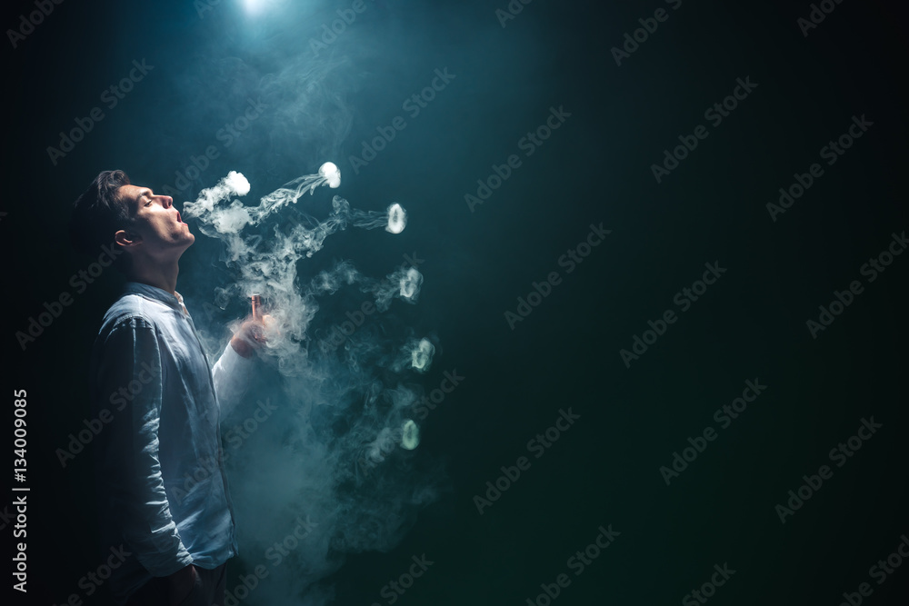 The man smoke an electrical cigarette with a ring and on the black background The man smoke an electrical cigarette with a ring and on the black background