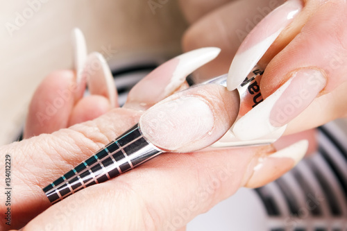Manicure specialist care by finger nail in beauty salon. Manicurist uses professional manicure tool.  Use of a template  schablon  for acrylic nails