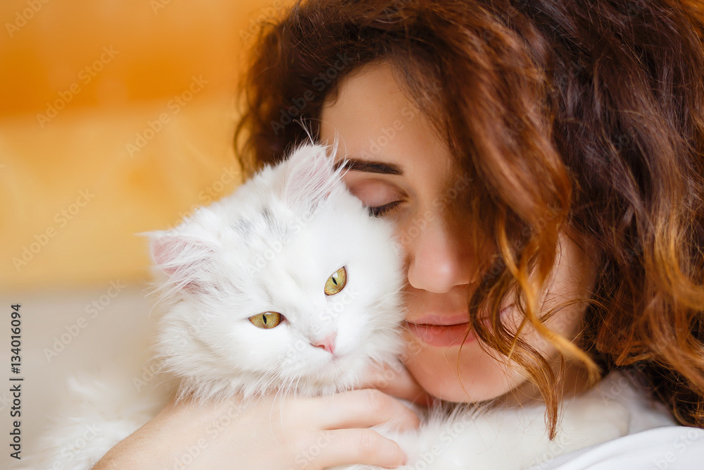 Cute girl with curly hair hugging white fluffy cat
