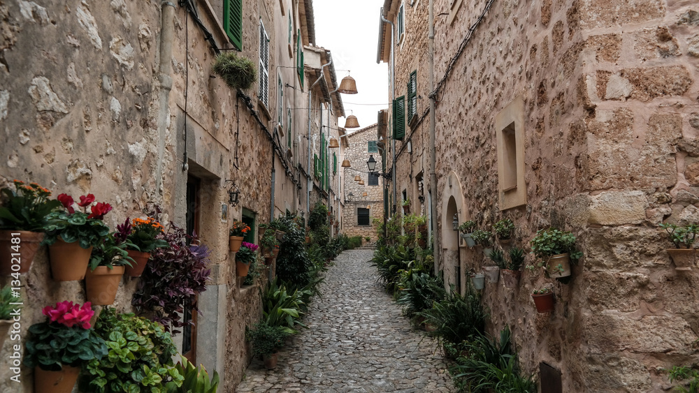 empty narrow street in Valldemossa Mallorca with typical historic houses on both sides and mountains in far distant background