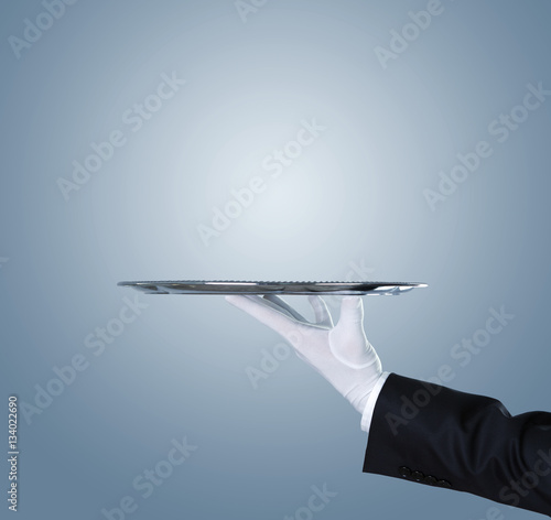 Waiter holding empty silver tray over blue background