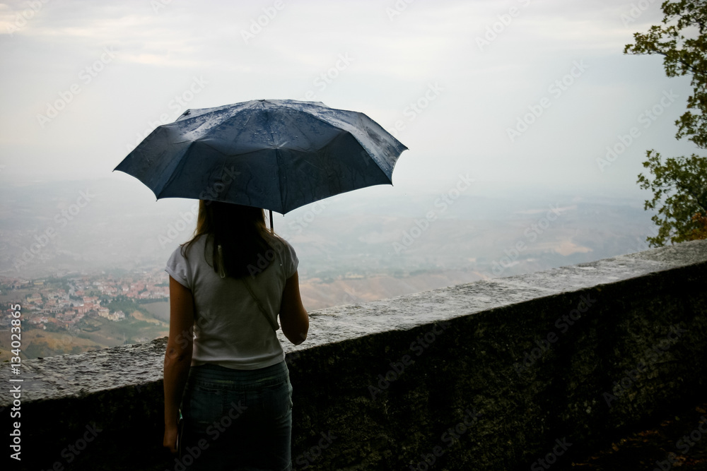 The girl under an umbrella looking over the valley in a rainy day.
