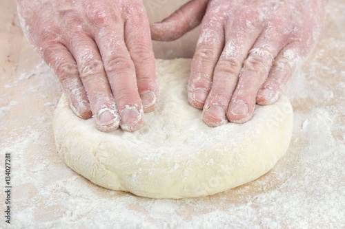 Pizza baking , starting to stretching dough on floured wooden board