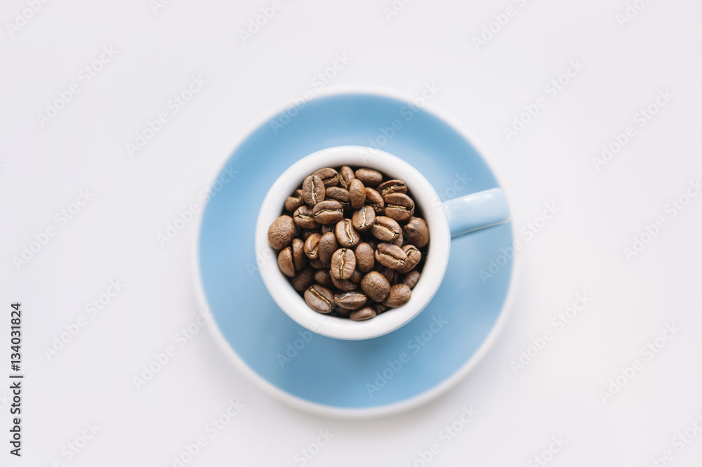 macro view of a blue espresso cup filled with freshly roasted coffee beans on a white background macro view of a blue espresso cup filled with freshly roasted coffee beans on a white background