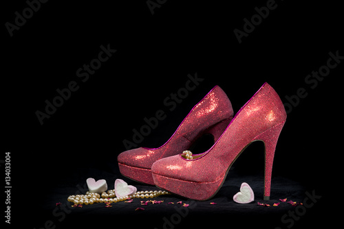 Pink party shoes and hearts on black background.