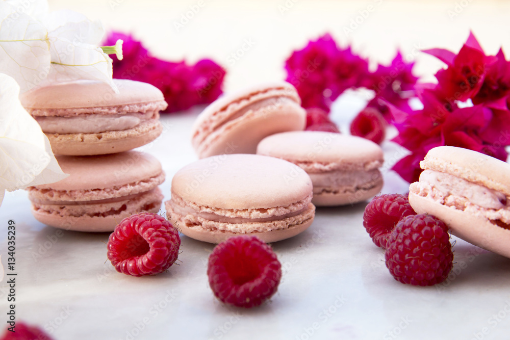 Delicious pink biscuits macaroons on light background with fresh berries raspberry and red flowers. A romantic date. Gift for Valentine's day. Ideal for holiday of international women's day.