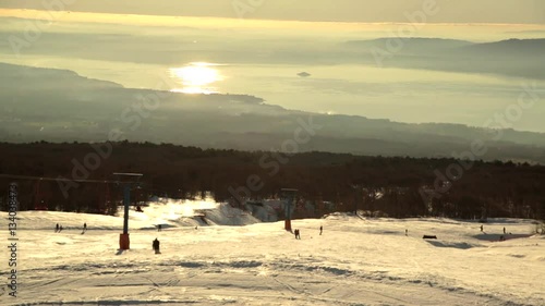 Skiers going down, with the sunset and lake on the background.