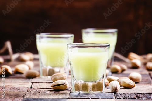 Pistachio liqueur in glass and nuts, vintage wooden background, photo