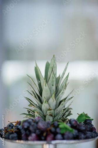 Stem of ananas stands on plate with dark grape