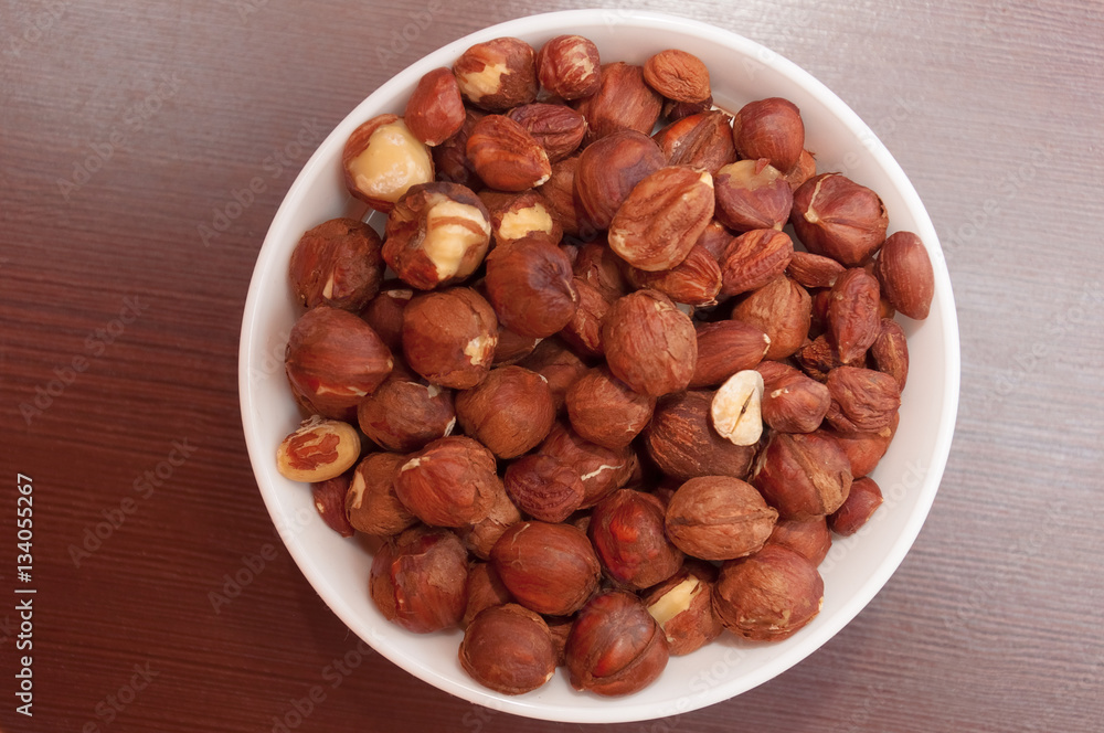 Hazelnuts in white bowl or cup at wooden background, top view. Hazelnuts in white bowl or cup at wooden background, top view.