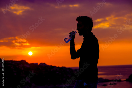 Profile of man silhouette drinking water from a bottle at sunset with the sun in the background