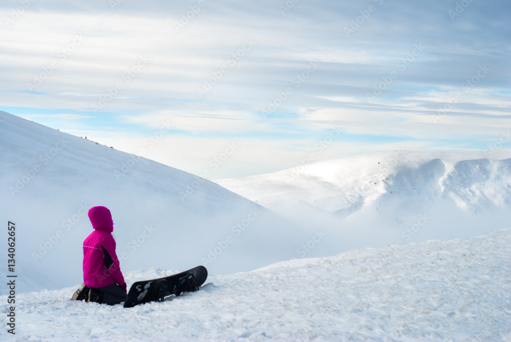 girl sitting with a snowboard on top of mountain