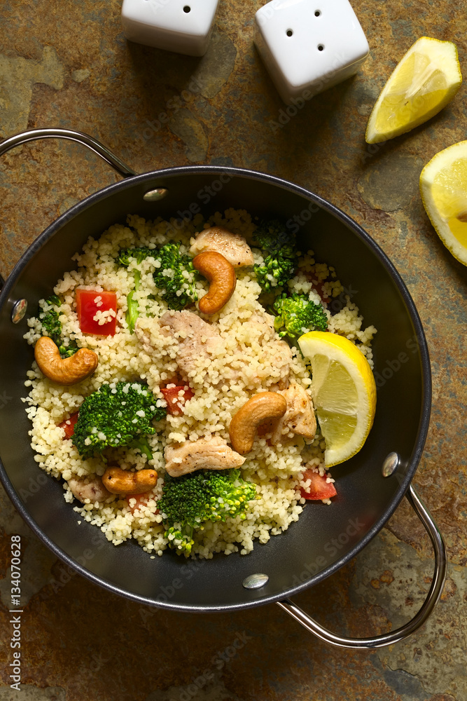 Couscous dish with chicken, broccoli, tomato, cashew nuts. Lemon, salt and pepper shakers on the side, photographed overhead on slate with natural light. Couscous dish with chicken, broccoli, tomato, cashew nuts. Lemon, salt and pepper shakers on the side, photographed overhead on slate with natural light.