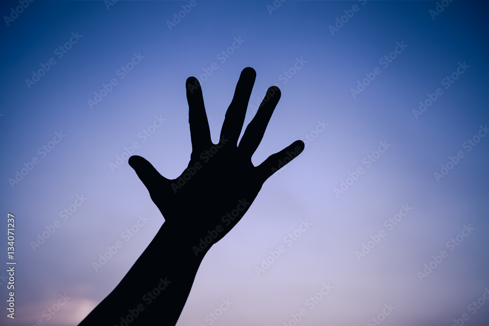Silhouette of a hand on colorful sky background.