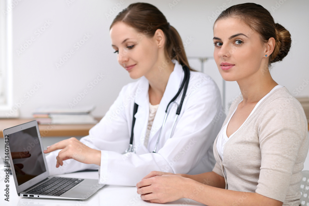 Doctor and patient sitting at the desk. Physician pointing into laptop computer. Medicine and health care concept Doctor and patient sitting at the desk. Physician pointing into laptop computer. Medicine and health care concept