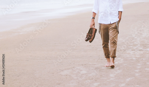 Alone man walking on the beach carrying leather shoes