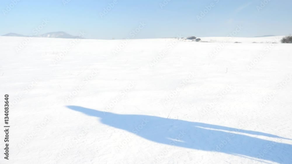 Winter tourist with snowshoes walk in snowy drift. Hiker in green sports jacket and black trekking trousers snowshoeing in powder snow. Amazing sunny winter day, gentle wind brings small snow flakes. 