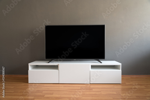 Flat LCD television on white cabinet in the living room with dark gray wall and parquet floor