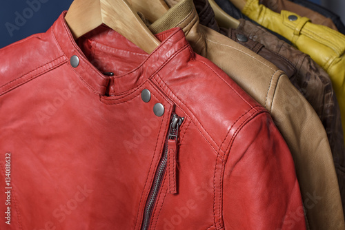 Many colored  leather jacket hanging on rack on blue background © sergmam