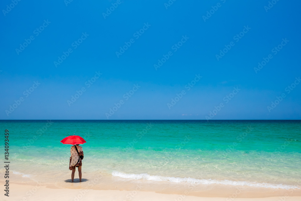 Girl with a red umbrella on the sandy beach.