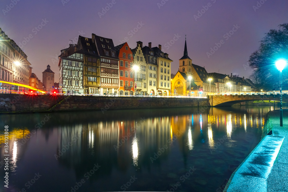 Picturesque quay and church of Saint Nicolas with mirror reflections in the river Ile during evening blue hour, Strasbourg, Alsace, France