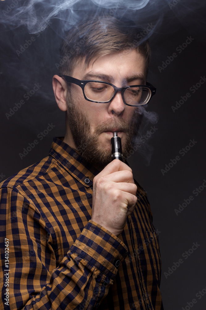 man with a beard wearing glasses on black background smoke Vape. large portrait of . electronic cigarette. E- for vaping. Popular devices the year - modern device. Stop smoking, man with a beard wearing glasses on black background smoke Vape. large portrait of . electronic cigarette. E- for vaping. Popular devices the year - modern device. Stop smoking,