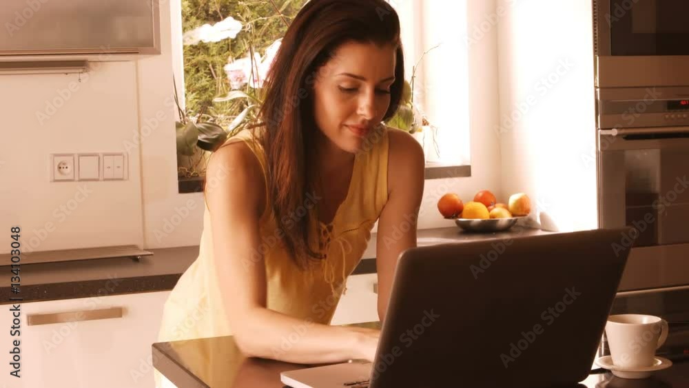 Woman using laptop in kitchen Woman using laptop in kitchen