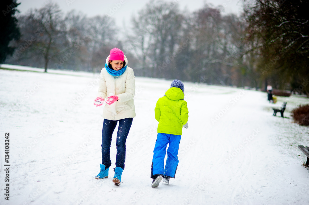 Young woman and her son cheerfully spend time in winter park.