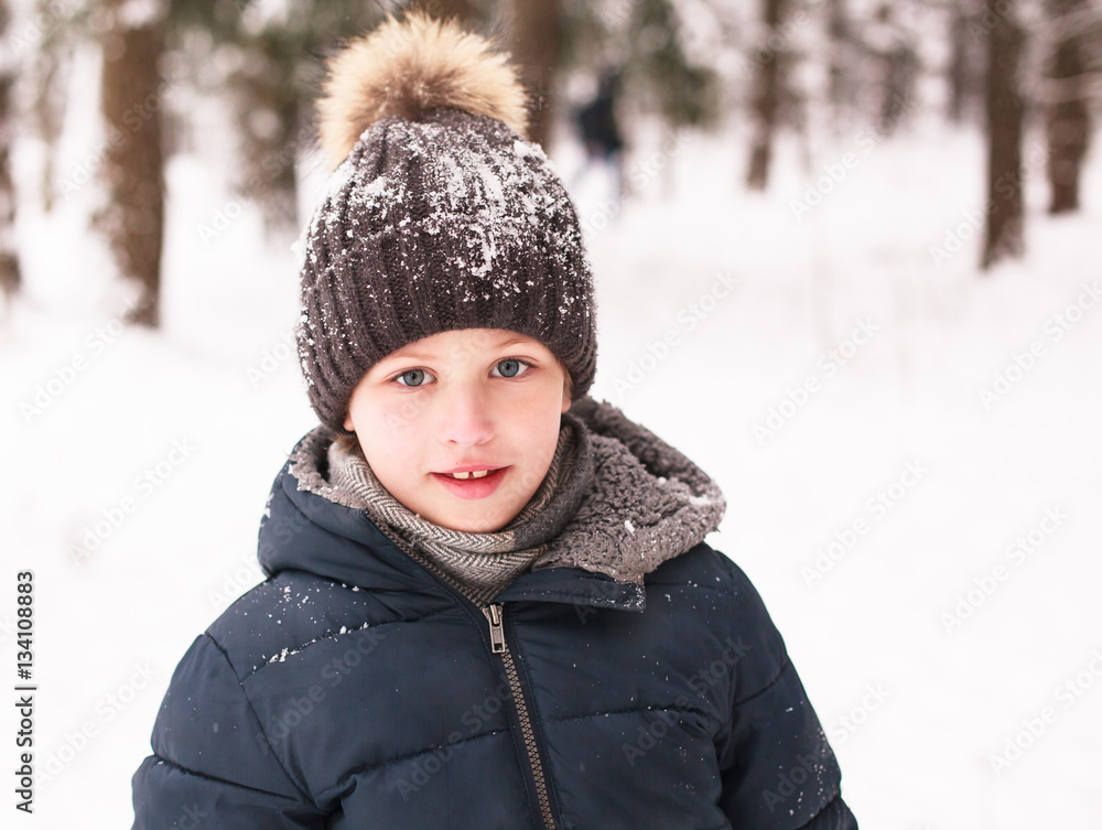 Portrait of cute boy wearing in warm hat with pom pom in winter forest 
