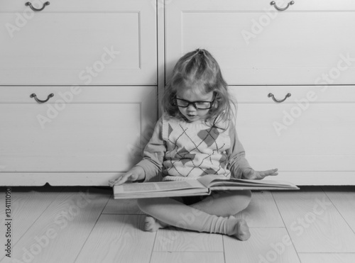 black and white, baby girl in glasses with book.